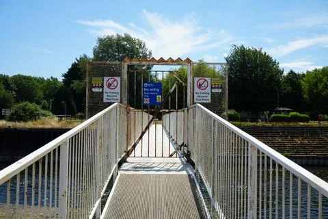 Rusty Pedestrian Bridge Over River With Warning Signs And Trees, Stock Photos