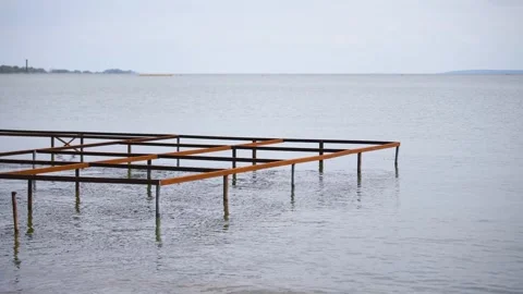 Rusty pier frame extending into calm gray sea under overcast sky with dista.. Stock Footage 344330387