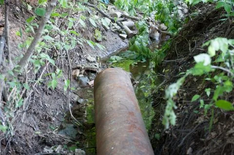 Rusty pipe feeds into a creek Stock Photos