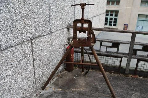 Rusty pipe vise on tripod stand beside textured wall and weathered balcony .. Stock Photos
