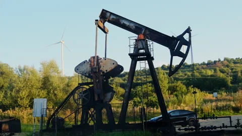 Rusty pumpjack works beside hillside and parked car Stock Footage 323885988