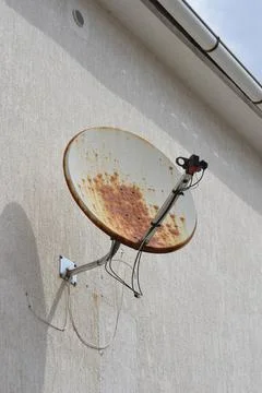 Rusty satellite dish mounted on a textured house wall Stock Photos