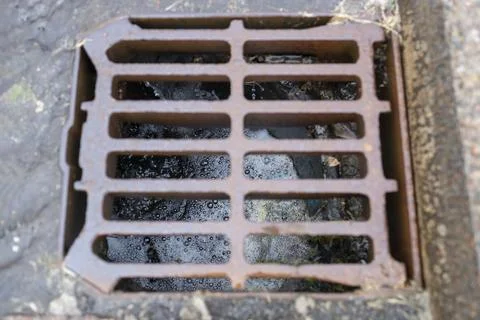 Rusty storm drain grate with rain water and debris flowing through with bubbles Stock Photos