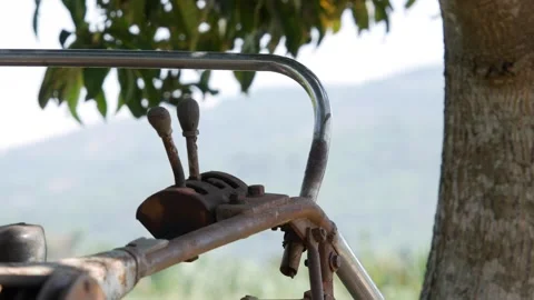 Rusty tractor controls and metal levers beside a field with trees and soft rural Stock Footage 339279954