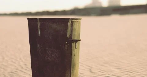 Rusty trash can on sandy beach at sunset reflecting natures neglect Stock Illustration