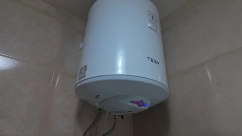 A rusty water heater leaks from its corroded tank and drips onto the floor Stock Footage 337507531