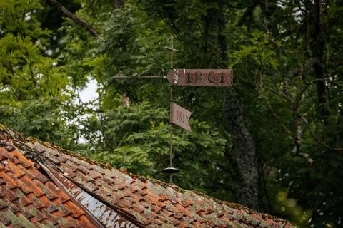 A rusty weather vane with dates 1861 and 1857 stands atop a mossy tiled roof Foto stock