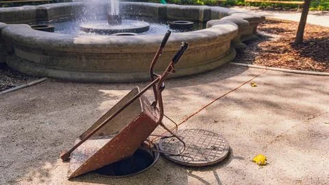 Rusty Wheelbarrow Over Open Maintenance Manhole in Park Stockfoto's