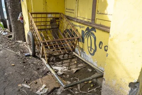 Rusty wheelbarrow is sitting in front of a yellow building Stock Photos