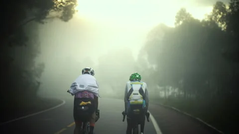 Rwanda - 3 September 2018: Two cyclists rides in the fog Stock Footage 138628083