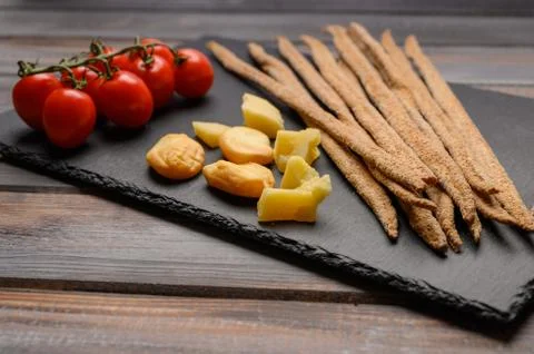 Rye bread grissini, cherry tomatoes, cheese and greens on a black cast iron Stock Photos