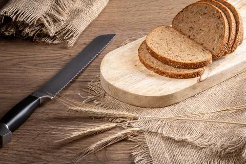 Rye bread, knife, ears of barley on a burlap napkin on the kitchen table Foto stock