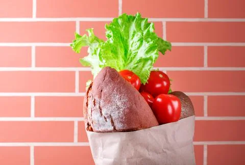 Rye bread, tomatoes and lettuce in craft paper bag by the brick wall Fotos Stock