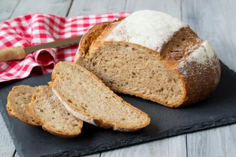 Rye round bread on stone cutting board with napkin, knife on wooden background Stock-Fotos