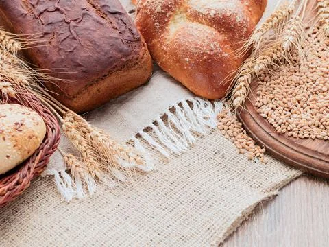 Rye spikelets, wheat bread, bun in the basket. Canvas, burlap, wooden table.. Stock Photos