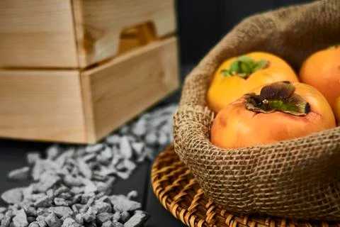 Sack of persimmons in the foreground on a gray background, with stones and a Stock Photos