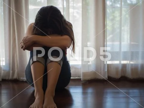 Sad and despaired woman hug her knee and cry while sitting alone on the floor Stock Photos