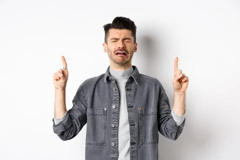 Sad and miserable guy crying while pointing fingers up, showing disappointed Stock Photos