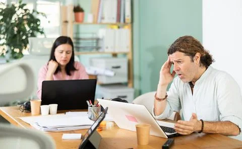 Sad and puzzled man working on laptop with problems in office Stock Photos