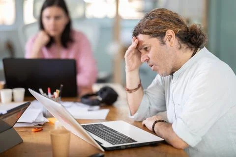 Sad and puzzled man working on laptop with problems in office Stock Photos