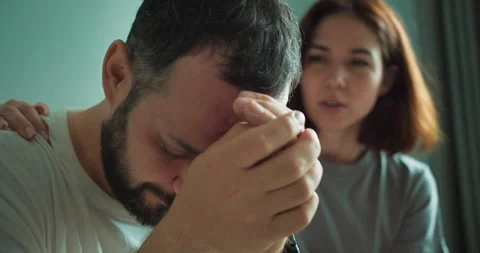 A sad and tired brunette guy with a beard leans on his hands and the girl tries Stock Footage 280664023