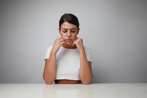 Sad and upset young woman deep in thought, posing over white background. Stock Photos
