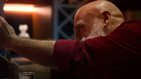 Sad bearded man in his 50s pours alcohol into glass, coping with depression Stock Footage 346714191