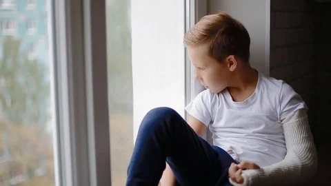 Sad boy with broken hand looking at the window Stock Footage 84137562