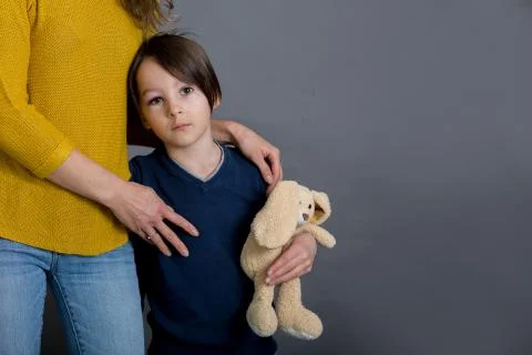 Sad boy with bruised eye, hugging mom and teddy bear at home Stock Photos