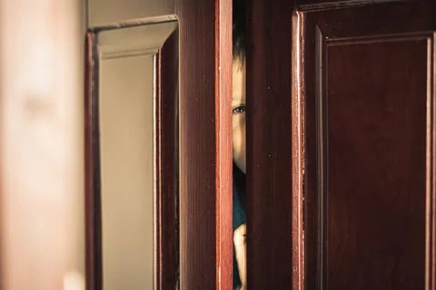 Sad boy hide in closet, close-up view of blue eye in ajar door slit home Stock Photos