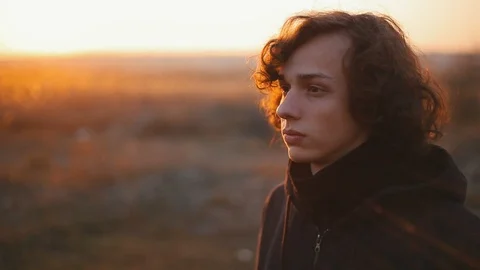 Sad boy looking far in the field at sunset. Close up Видео 98749634