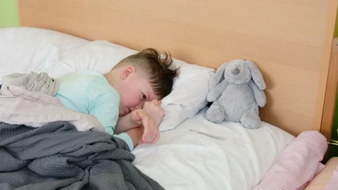 A sad boy is lying on the bed and measuring the temperature with a mercury Stock Footage 171087612