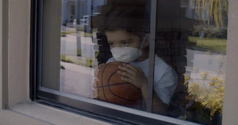 Sad boy playing with his ball and looking out the window by quarantined by th Stock Footage 128996323