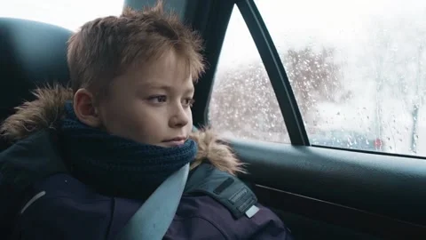 Sad boy rides in the car in the back seat in winter and looks out the window Stock Footage 87352327