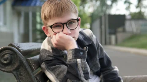 A sad boy sits on a bench in a bad mood near the school. Childhood depression. Stock Footage 312199882