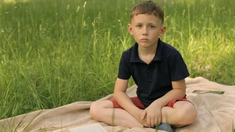 Sad boy sitting in the park on a meadow Stock Footage 76097261