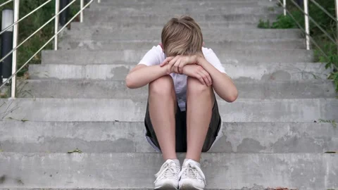 Sad boy sitting on the steps of the stairs. Childhood depression. Stock Footage 288972756