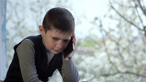 Sad boy talking on phone at window in rainy weather Video stock 74772775