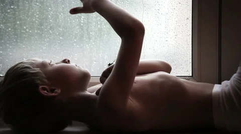Sad boy on the windowsill watches the raindrops on the glass Stock Footage 44334658