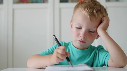 Sad boy writing in a notebook with a pen. Tired little child studying in cl.. Stock Footage 340729077