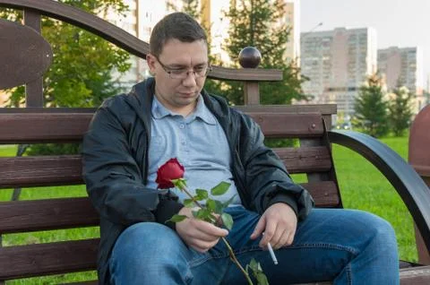 A sad, brooding, upset guy with a smoking cigarette and a red rose in his hand Stock Photos