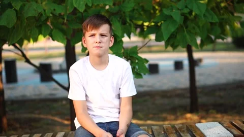 Sad calm boy sits alone in the park. close-up portrait. Stock Footage 248377403