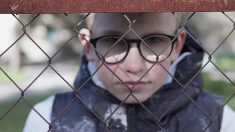 Sad child looking over school fence. Bullying and childhood depression. Stock Footage 311447510