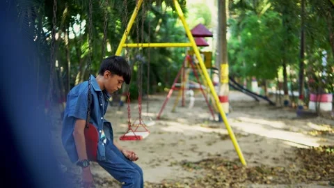 Sad child sitting alone on a swing in a playground Stock Footage 312689979