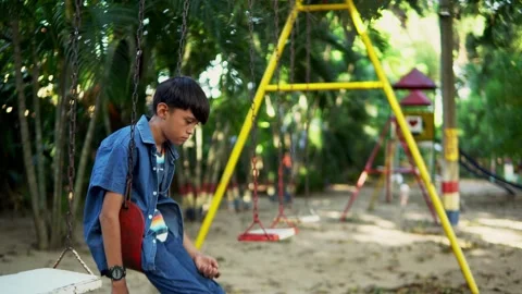 Sad child sitting motionless on a swing in a playground Stock Footage 312690006
