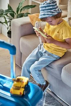 A sad child is sitting on a sofa using a mobile phone and waiting for departure Stock-Fotos