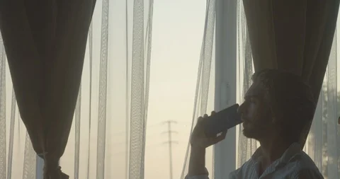 Sad crying man having an intense conversation on phone next to window at dusk 3 库存影片 128522916