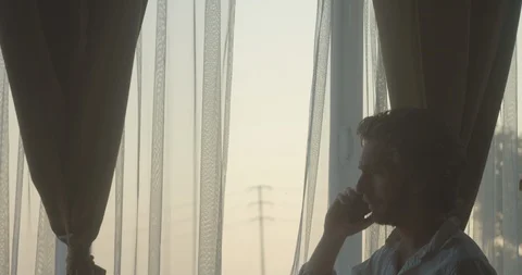 Sad crying man having an intense conversation on phone next to window at dusk 库存影片 128524187