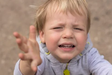 Sad crying toddler pulls his hands up. Close up portrait of baby boy asking for Stock Photos