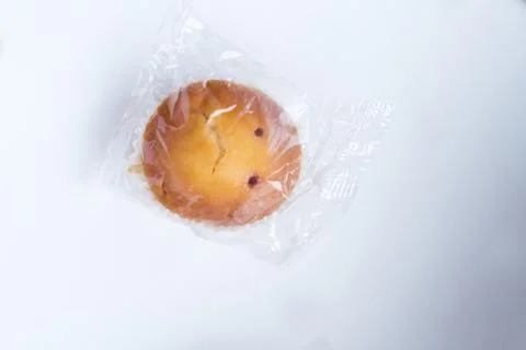 Sad cupcake in packaging on a white background. Cupcake with a sad face. Stock Photos